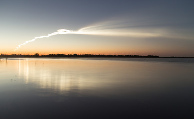 Smoke trail from a rocket at sunset with reflection in water