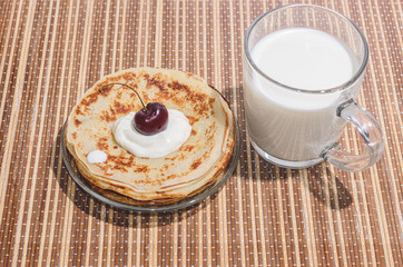 Russian traditional dishes - pancakes  with cherry and cream on a plate and milk  on a bamboo napkin