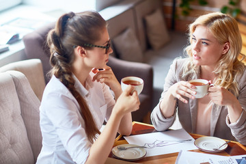 Pretty young colleague taking short break from work and enjoying herbal tea and pleasant conversation in cozy small cafe