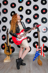 Sexy woman in a sequin dress, leather jacket and red lips. Disco style. Girl hipster playing the guitar.