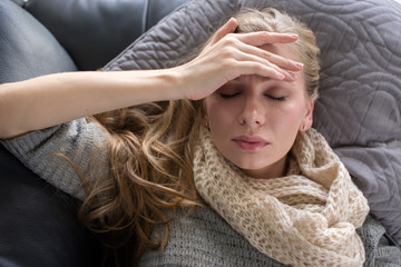 woman has a fever and lying down on the sofa with closed eyes
