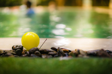 Colorful ball toys on small stone with blur pool water background, swimming pool , Morning sunshine.
