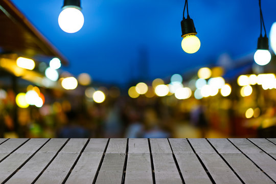 Image Of Wooden Table In Front Of Decorative Outdoor String Lights Hanging On Electricity Post In Night Market With Blur People. Christmas, Festival And Holiday Concepts