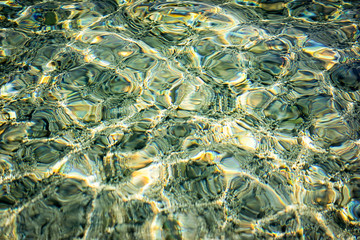 Fototapeta na wymiar texture of sunlight at the water surface at the sea pebble shore.