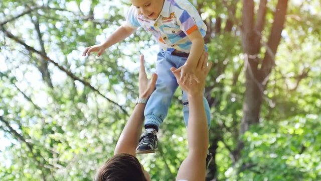 Young father with baby boy enjoying sunny day in the park in slow motion. Dad holds boy in hands throwing his in an air. Happy childhood and parenthood. 1920x1080