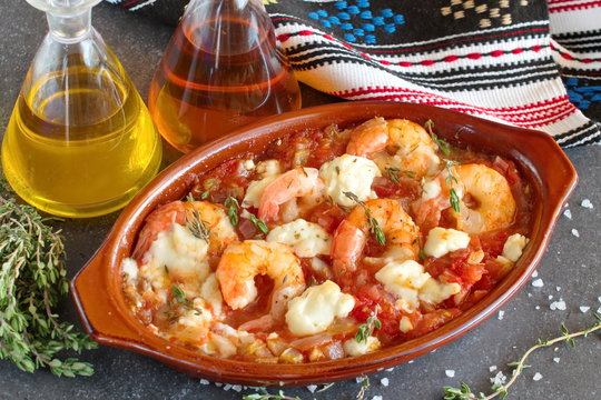 Oven backed prawns with feta, tomato, paprika, thyme in a traditional ceramic form on a abstract background. Healthy eating concept. Mediterranian lifestyle.