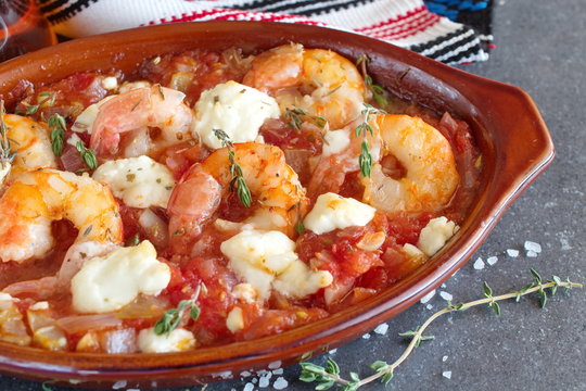 Oven backed prawns with feta, tomato, paprika, thyme in a traditional ceramic form on a abstract background. Healthy eating concept. Mediterranian lifestyle.