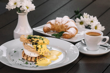 Poached eggs sandwich for breakfast with croissant,  coffee and chamomile on dark wood background