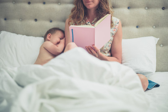 Mother in bed with baby reading from diary