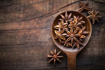 Star anise in a spoon on dark rustic wooden background. Overhead view with copyspace for your text