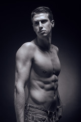 Fototapeta na wymiar one young adult man, Caucasian, fitness model, muscular body, shirtless, jeans, black background, studio, posing, looking sideways, monochrome, black and white image