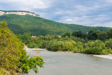 Shore of the mountain river Ashe with green trees, mountains and the sky at the background. Krasnodar region, Adygea, Russia