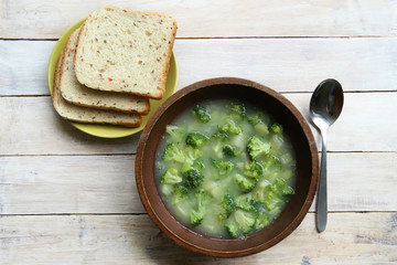 Broccoli soup on wooden table. Broccoli soup in bowl with bread in plate top view.
