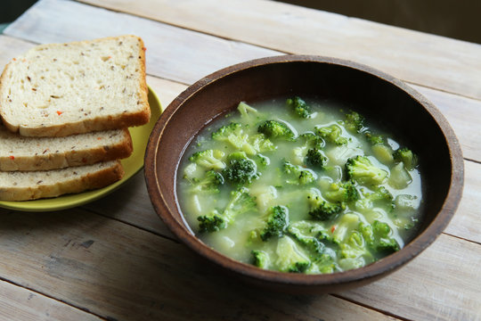 Broccoli soup on wooden table. Broccoli soup in bowl with bread in plate.