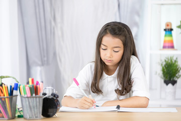 Cute Asia girl writing something in paper with colour pencils