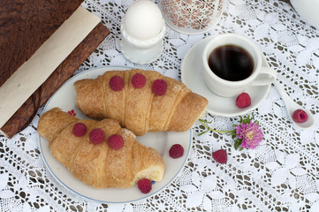 Breakfast with cup of coffee. A dessert with croissants and berries of raspberry on white a lace tablecloth. Top view