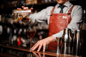 close up bartender pouring bright red alcohol cocktail into fancy glass