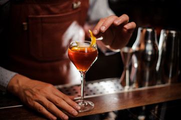 Bartender with glass and lemon peel preparing cocktail at bar