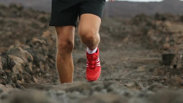 Trail runner man running - Close up of running shoes. Young male athlete jogging in volcano landscape. Determined man exercising in sportswear on rocky field during sunny day.
