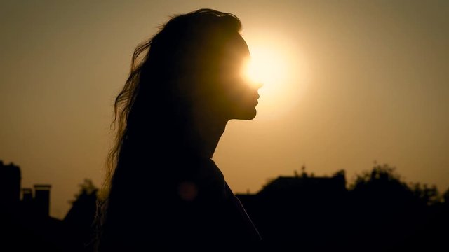 young slim woman with long wavy hair is walking in evening time in countryside, close-up portrait against the sun
