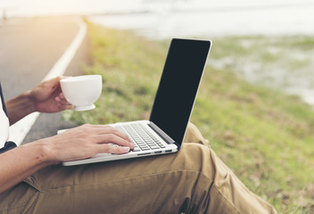 Close up hands of handsome man using laptop holding cup of coffee at outdoor cafe. Freelance working outdoor. Lifestyle new generation work as a freelance.