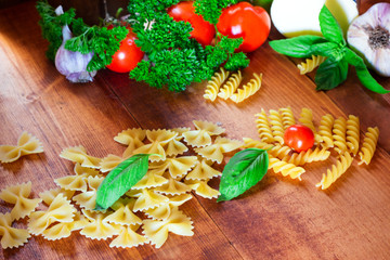 Italian food background with uncooked pasta, tomato, basil, cheese, garlic on rustic wooden table Ingredients for cooking pasta with space for recipe.