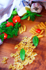 Italian food concept .Various kind of pasta with ingredients sweet basil, tomato, garlic, parsley, pepper and cheese on rustic wooden background flat lay.