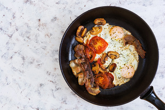 Fried eggs with bacon, tomatoes and mushrooms on white background. Top view