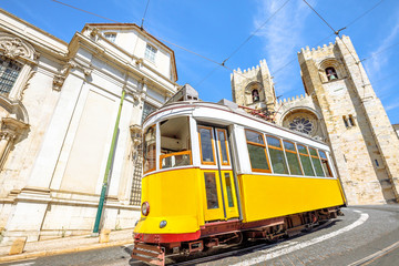 Fototapeta na wymiar Historic tram line in front of Lisbon Cathedral in Alfama district, Lisbon, Portugal. Lisbon street with typical yellow vintage tram and Se de Lisboa. Icons and symbols of the Portuguese capital.