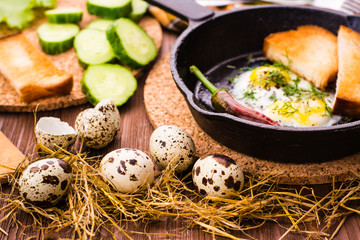Quail eggs and scrambled eggs in a iron pan on a wooden table