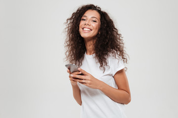 Smiling curly woman with smartphone in hands looking at camera