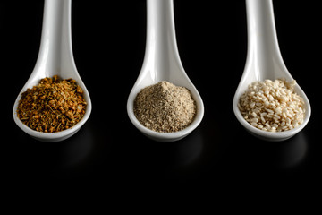 porcelain spoons with spices on a black background isolated