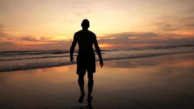 Silhouette of man walking on beach during sunset, super slow motion 240fps
