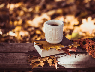 Hot coffee and red book with autumn leaves on wood background