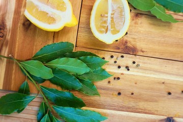  Fresh bay leaves and lemon lay on wooden cutting board.