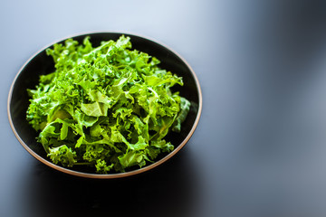 Fresh green kale salad leaves in a bowl on black board with copy space for text background.