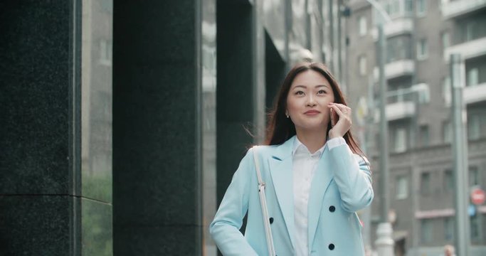 Steadicam shot of a young beautiful Asian girl in a great mood, emotionally speaks on the phone on the way to work