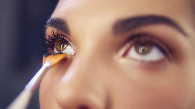 Professional make-up artist applying eyeshadow to model eye using special brush. Natural makeup in salon. Beauty, makeup and fashion concept. Slowmotion shot