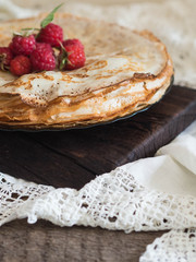 Stack fried crepes with raspberries on dark board. Russian-style