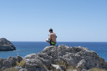young man crouching on a rock with mobile phone