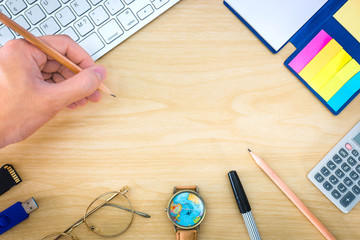 Top view, Hand holding a pencil over office desk with notepad, calculator, glasses and watch, copy space.
