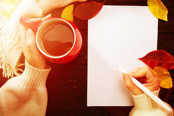 Woman's hand holding a red cup of coffee above dark wooden table. woman going to write.