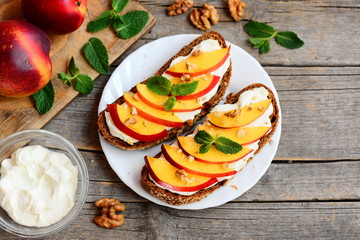 Vegetarian sandwiches with cream cheese, nectarines, walnuts and mint on a serving plate and on an old wooden background. Healthy lunch sandwiches idea. Closeup. Top view