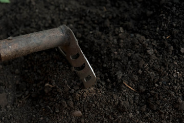 an old shovel stuck into the black earth dug in the garden.