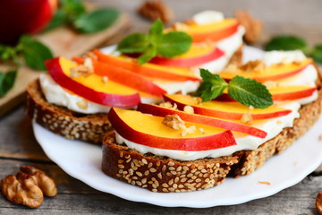 Sandwiches with cream cheese, nectarines, walnuts and mint on a serving plate and on an old wooden table. Healthy sandwiches idea. Closeup