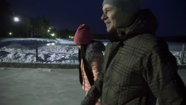 Young couple holding hands and rolling on ice at night