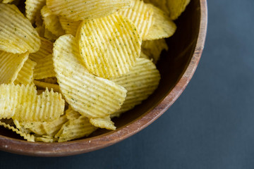 Potato chips in bowl on a grey background, top view. Salty crisps scattered on a table