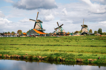 Fototapeta premium Panoramic view of Authentic Zaandam mills in Zaanstad village on the river Zaan against the sky with clouds. Landmark of Netherlands.