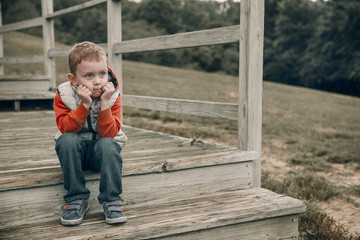 pensive boy sitting on wooden steps. child patiently waiting on the stairs. Copy space for your text