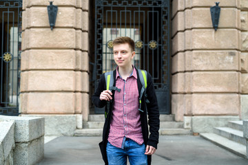 Portrait of stylish young man in plaid shirt and jacket with backpack walking in the city outdoors. Student travel, free space